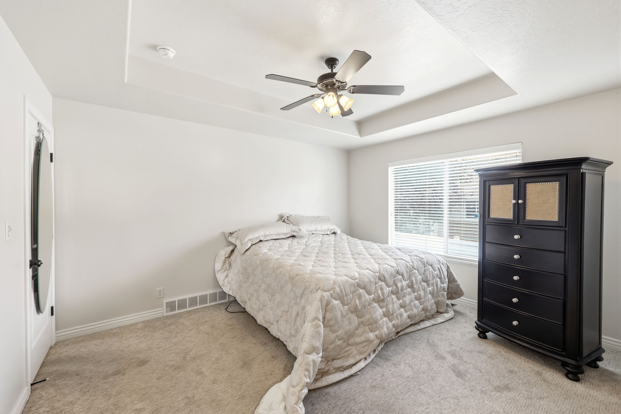 Bedroom featuring a tray ceiling, ceiling fan with light fixture, window with blinds, and neutral carpet flooring