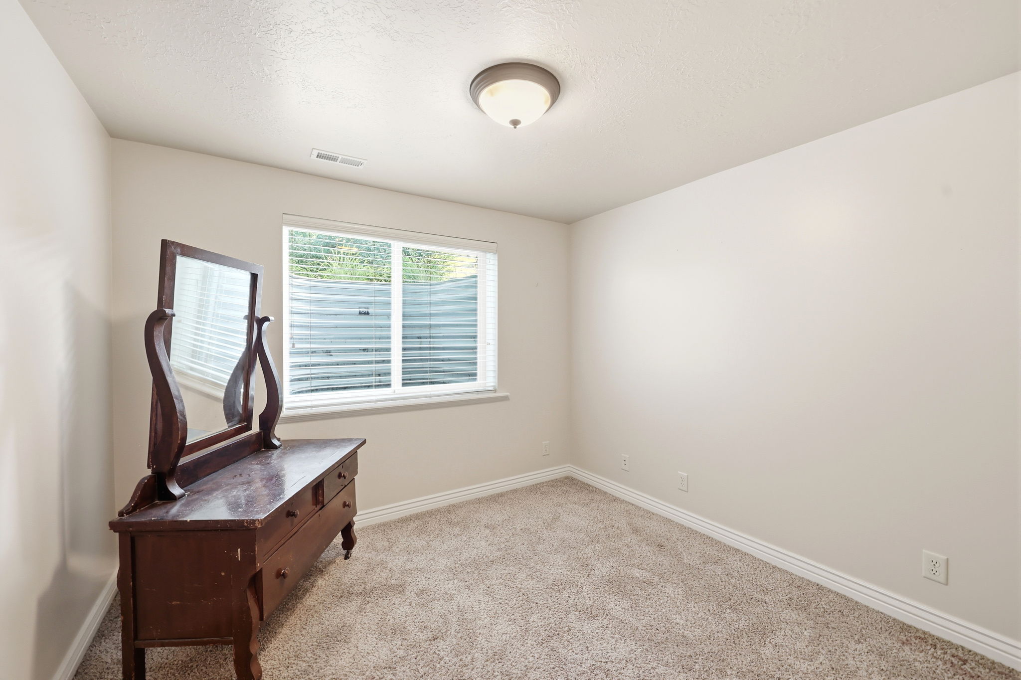 Spacious room featuring neutral carpeting, light-toned walls, and a window with horizontal blinds