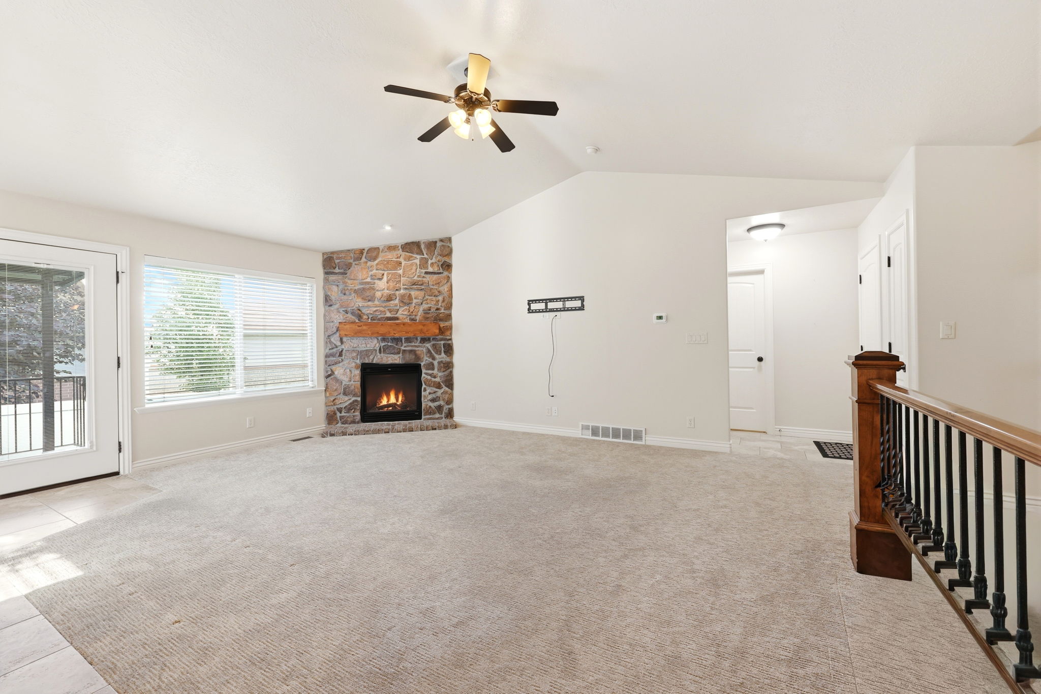Spacious living area featuring vaulted ceilings, a corner fireplace with a stone surround and wood mantle, and light-colored carpeting