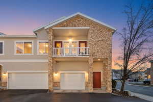 View of front of property with stone siding, a balcony, stucco siding, and asphalt driveway