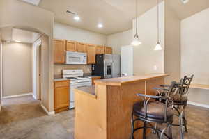 Kitchen with white appliances, a peninsula, a breakfast bar area, hanging light fixtures, and light countertops