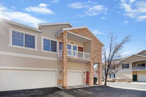 Traditional-style home featuring a balcony, stucco siding, stone siding, an attached garage, and driveway