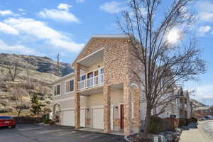 View of side of property with a balcony, a garage, stucco siding, stone siding, and driveway
