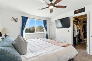 Carpeted bedroom with a walk in closet and a ceiling fan
