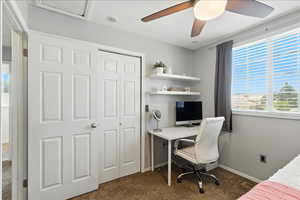 Bedroom with dark colored carpet, an office area, a closet, and ceiling fan