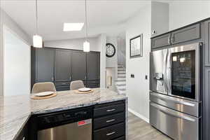 Kitchen with stainless steel appliances, light stone counters, hanging light fixtures, light wood-type flooring, and lofted ceiling