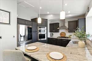 Kitchen featuring a breakfast bar area, vaulted ceiling, light stone countertops, stainless steel appliances, and hanging light fixtures