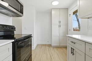 Kitchen with black electric range oven, stainless steel microwave, white cabinets, and light wood finished floors