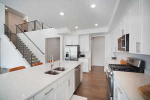 Kitchen featuring stainless steel appliances, light stone counters, white cabinets, recessed lighting, and dark wood-style flooring