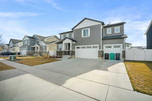 Craftsman-style home featuring an attached garage, a gate, stone siding, driveway, and board and batten siding