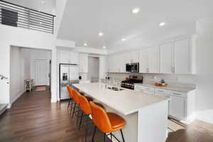 Kitchen with stainless steel appliances, dark wood-style flooring, white cabinets, a kitchen bar, and a center island with sink