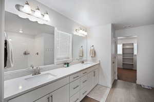 Bathroom with double vanity, walk in shower, a walk in closet, and dark tile patterned floors