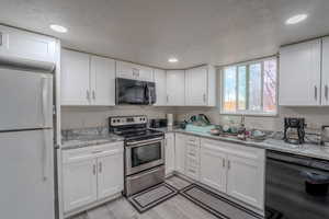 Kitchen with black appliances, white cabinets, recessed lighting, light stone counters, and a textured ceiling