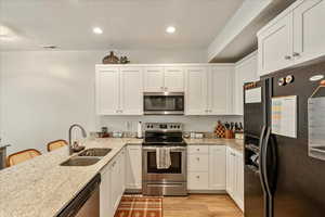 Kitchen featuring stainless steel appliances, a kitchen breakfast bar, white cabinetry, light stone counters, and a peninsula