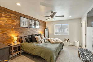 Bedroom with an accent wall, light carpet, wood walls, a textured ceiling, and recessed lighting