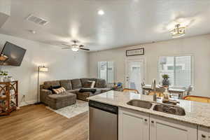 Kitchen with open floor plan, dishwasher, white cabinets, light stone countertops, and a textured ceiling