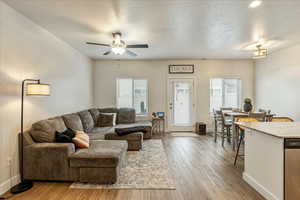 Living area featuring a textured ceiling, light wood finished floors, a ceiling fan, and healthy amount of natural light