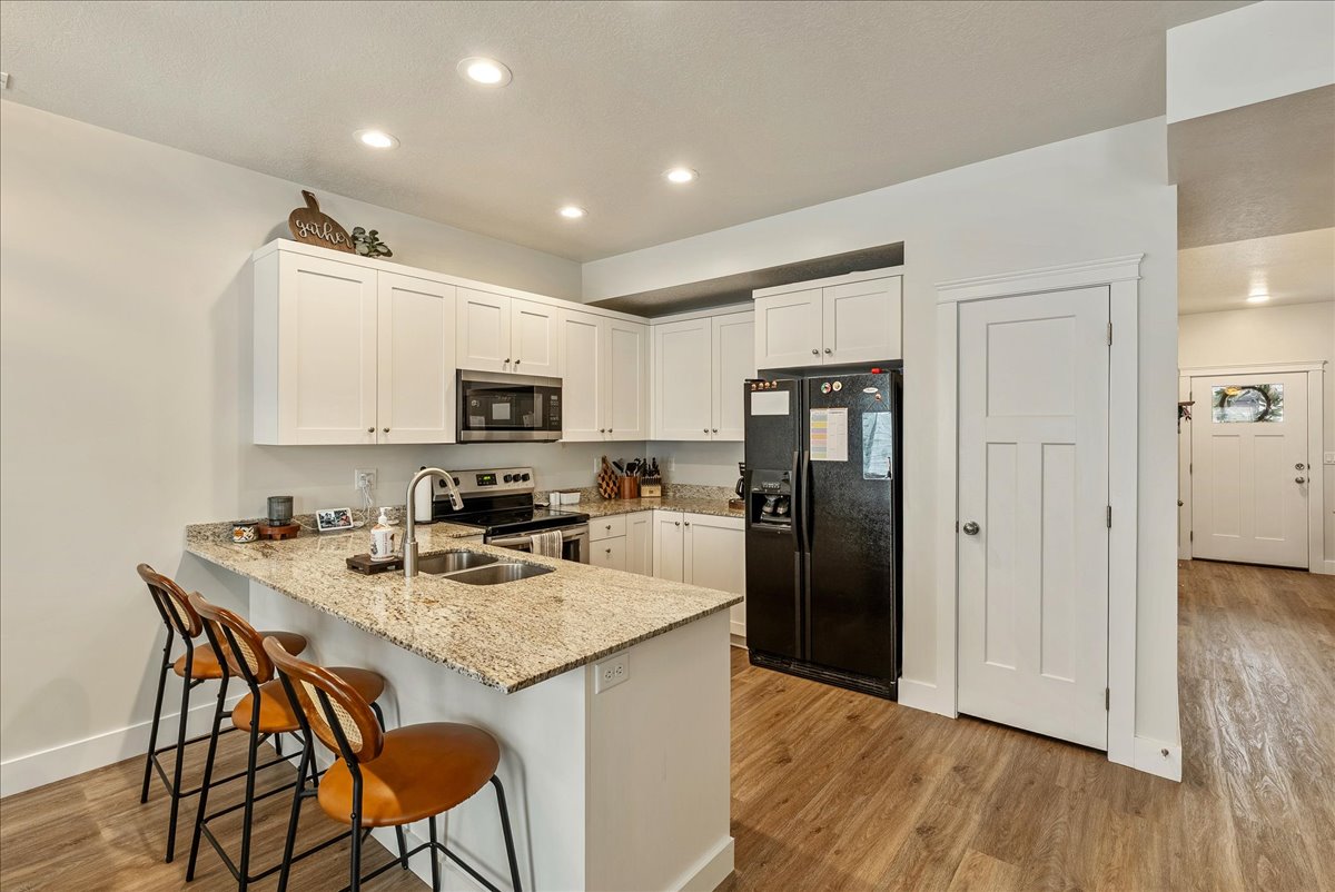 Kitchen featuring light stone counters, a peninsula, stainless steel appliances, a kitchen bar, and white cabinets
