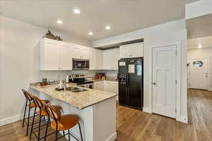 Kitchen featuring light stone counters, a peninsula, stainless steel appliances, a kitchen bar, and white cabinets