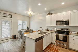 Kitchen featuring a peninsula, stainless steel appliances, a kitchen bar, white cabinets, and light stone countertops