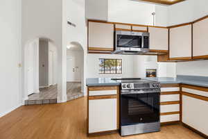 Kitchen featuring two tone color scheme, stainless steel appliances, a high ceiling, light wood-style floors, and a peninsula