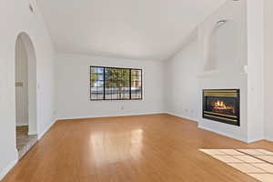 Unfurnished living room featuring lofted ceiling, light wood finished floors, arched walkways, and a glass covered fireplace