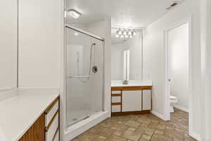 Full bathroom with a textured ceiling, vanity, stone finish floors, and a shower stall