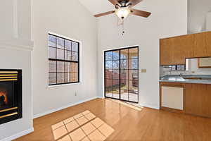 Unfurnished living room featuring a glass covered fireplace, light wood-style flooring, a ceiling fan, a high ceiling, and healthy amount of natural light