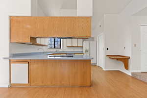 Kitchen with light countertops, white fridge with ice dispenser, a peninsula, light wood-type flooring, and stainless steel cooktop