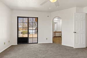 Unfurnished bedroom featuring arched walkways, access to outside, a textured ceiling, carpet flooring, and ceiling fan