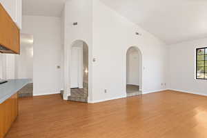 Unfurnished living room featuring vaulted ceiling, light wood-style floors, and arched walkways