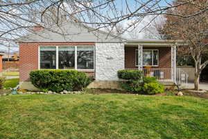 View of front of property with covered porch, a front lawn, brick siding, and a chimney