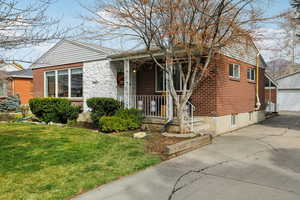 View of front of home with brick siding, an outdoor structure, a porch, a front yard, and a detached garage