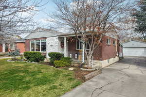 View of front of property featuring an outdoor structure, a porch, a detached garage, brick siding, and a front lawn