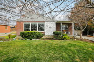 View of front of home featuring a front lawn, brick siding, and covered porch