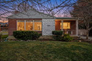 View of front of property featuring covered porch, a lawn, and brick siding