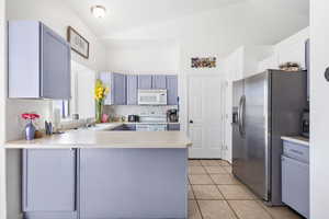 Kitchen featuring white appliances, light countertops, lofted ceiling, a peninsula, and light tile patterned floors