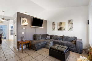 Living area with vaulted ceiling, a ceiling fan, and light tile patterned floors