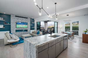 Kitchen with an island with sink, light wood-style flooring, open floor plan, gray cabinets, and a fireplace