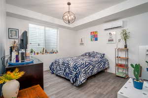 Bedroom with wood finished floors, suspended lighting, and a mini split for heating / cooling