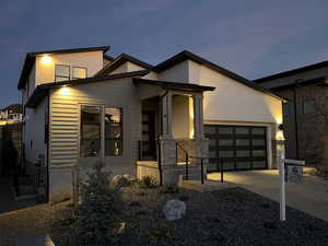 Modern home featuring an attached garage, concrete driveway, stone siding, and stucco siding