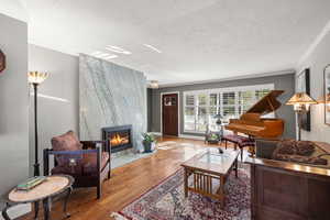 Living room featuring oak floors, a large fireplace, a textured ceiling, and crown molding