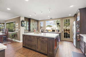 Kitchen featuring refrigerator, wood cabinetry, a kitchen island with sink, tile floors, and a textured ceiling