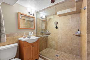 Full bathroom featuring vanity, walk in shower, tile walls, and a textured ceiling