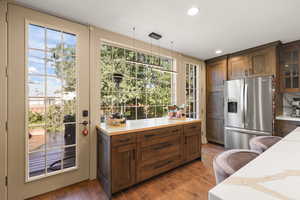 Kitchen with stainless steel fridge, glass insert cabinets, tile floors, pendant lighting, and wood cabinetry.