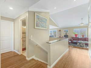 Hallway with an upstairs landing, crown molding, light wood finished floors, vaulted ceiling, and plenty of natural light