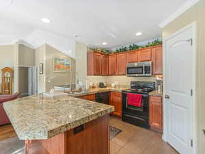 Kitchen featuring black appliances, a peninsula, wood finish cabinets, ornamental molding, and dark tile patterned floors