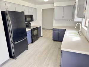 Kitchen with light countertops, black appliances, light wood-style flooring, and blue cabinets