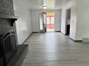 Unfurnished living room with a brick fireplace, wood finished floors, and a textured ceiling