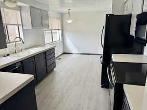 Kitchen with black appliances, light countertops, light wood finished floors, and a textured ceiling